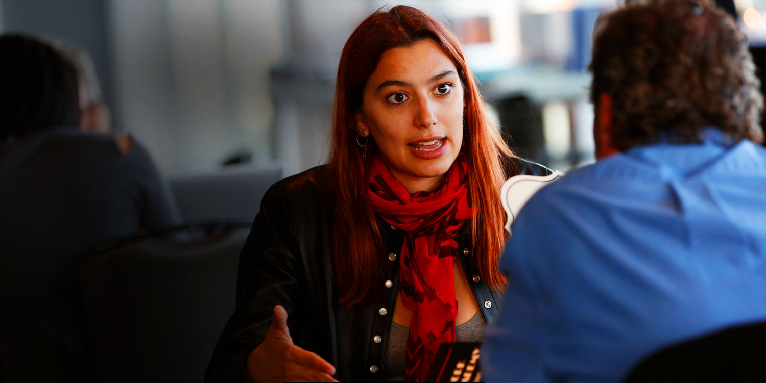 woman in red scarf and leather jacket sitting down and talking at new york film academy producing showcase